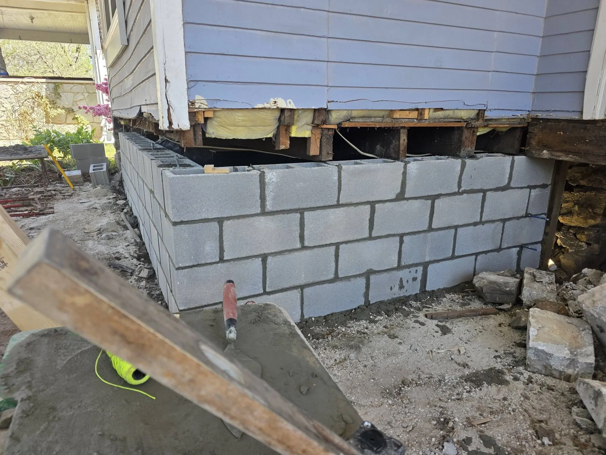 New concrete block foundation wall laid under the floor framing of an older house to replace a failing stone foundation