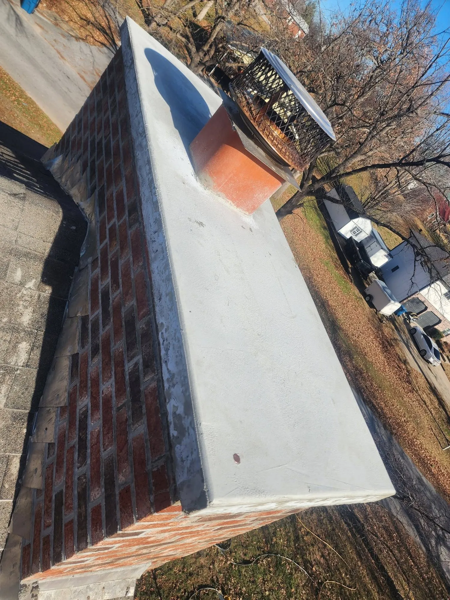 Freshly poured concrete chimney crown with flue tile and stainless steel cap on a brick chimney