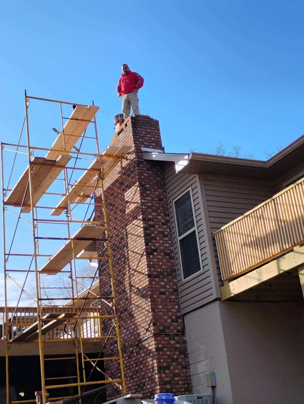 Tall brick chimney being rebuilt with scaffolding, owner standing on top