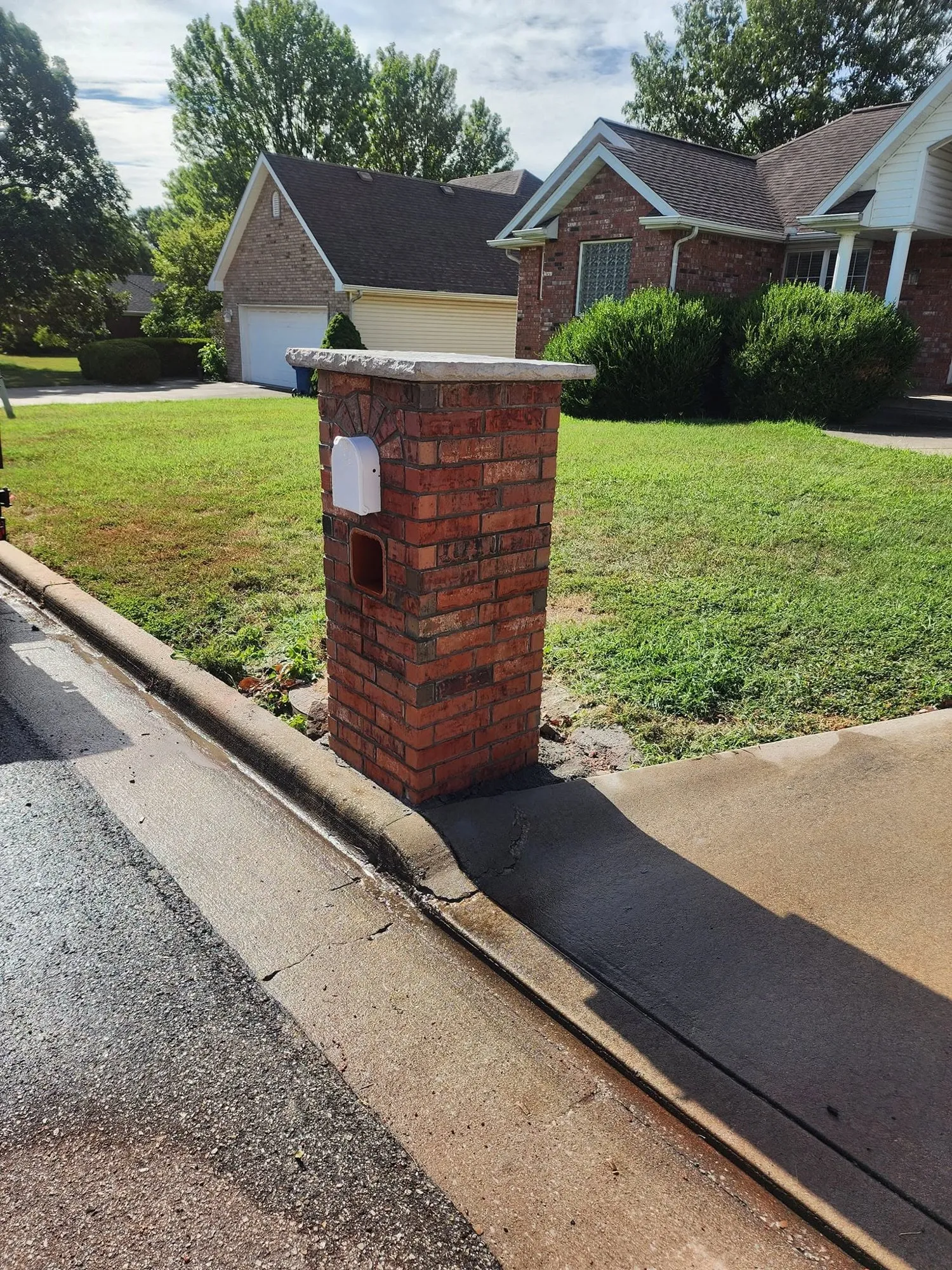 Brick mailbox column with arched brick detail, newspaper slot and rock-face stone cap at a curb