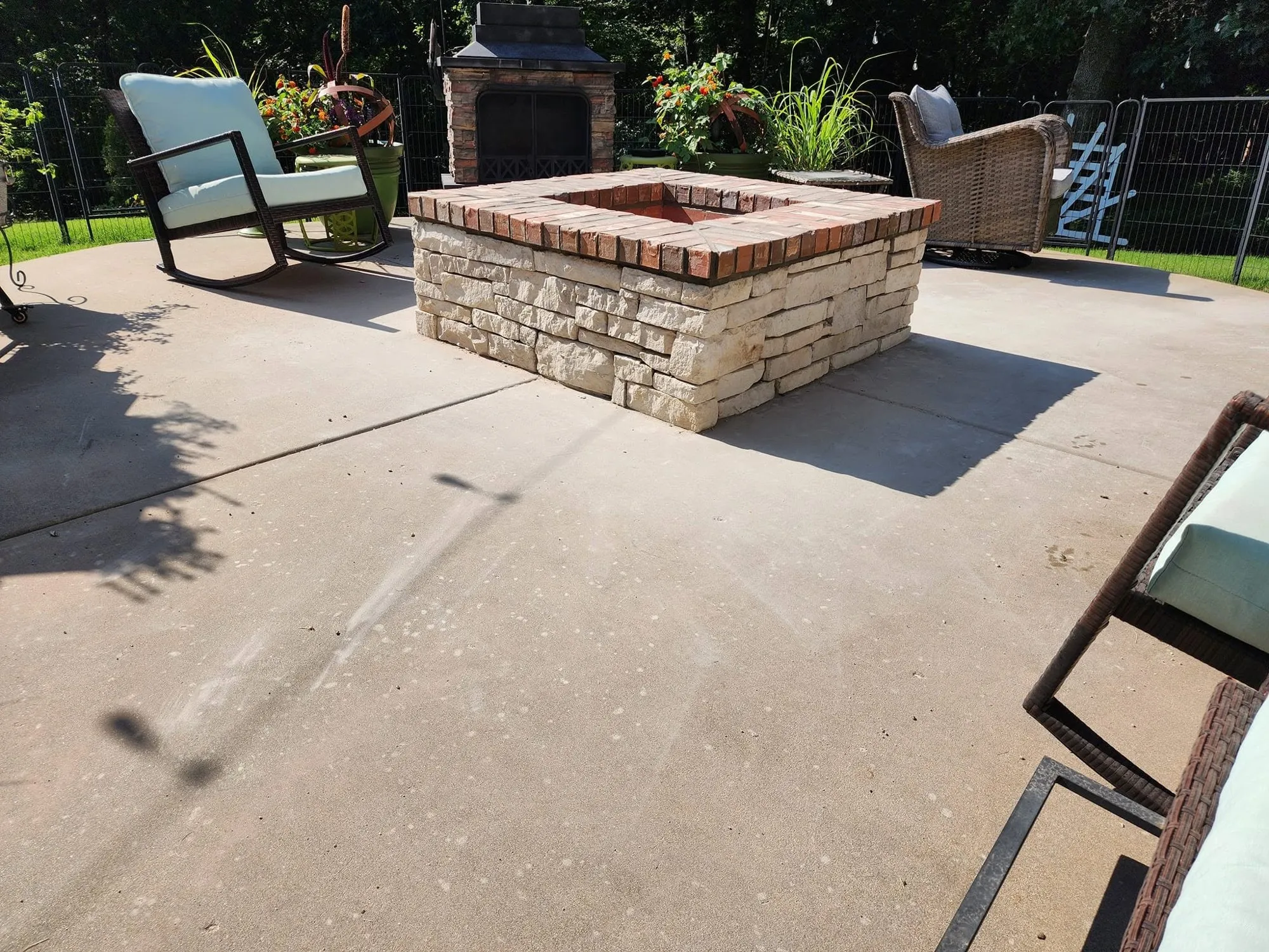 Limestone and brick fire pit surrounded by patio chairs on a backyard concrete patio