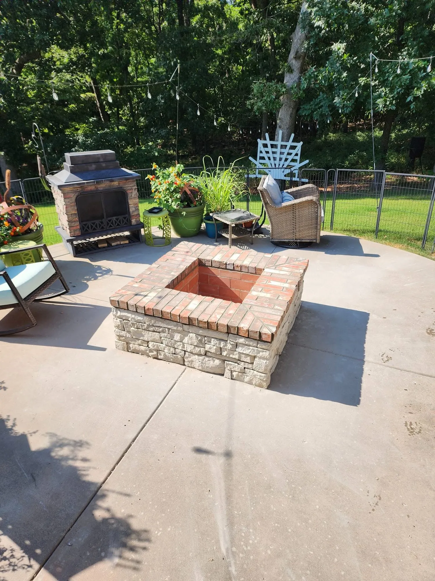 Square fire pit with stacked limestone sides and a red brick cap on a concrete patio