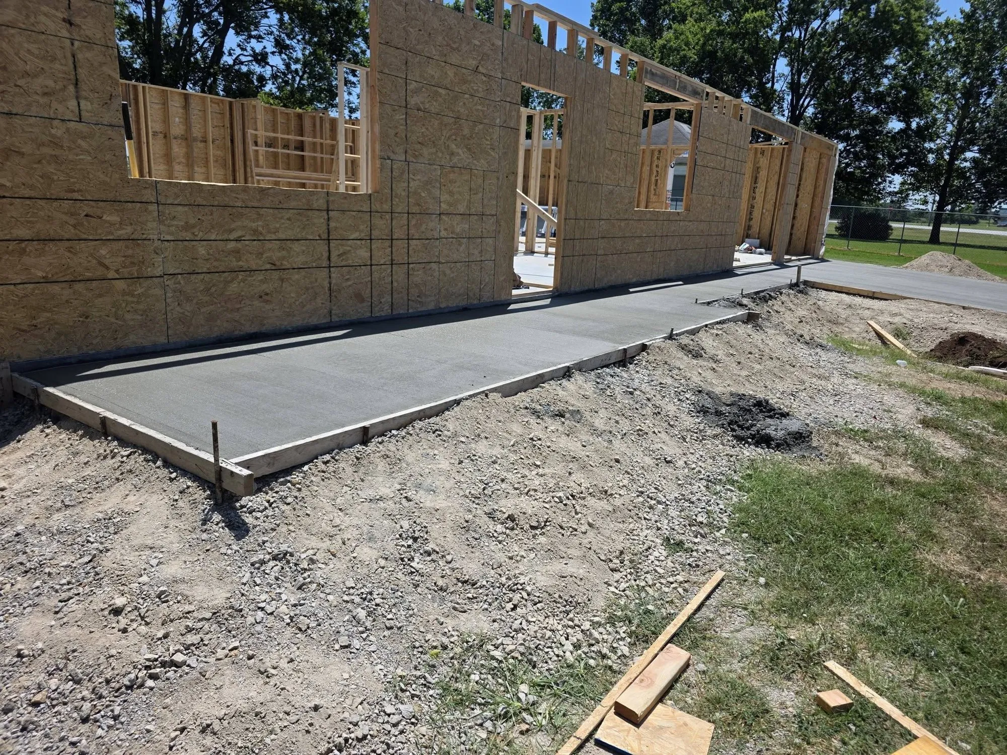 Freshly finished concrete sidewalk in forms along a newly framed building