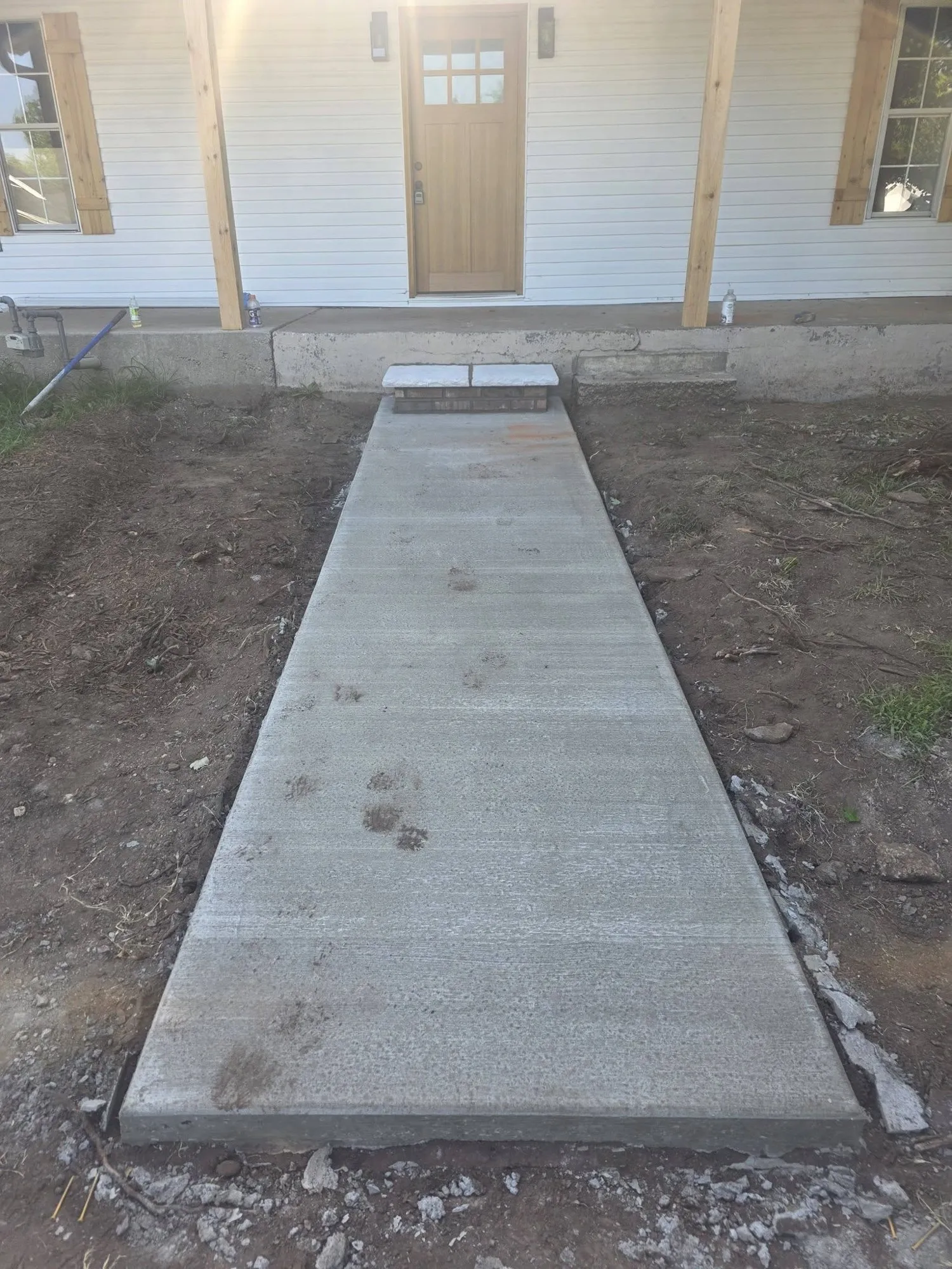 New broom-finished concrete walkway leading to a brick step with stone cap at a front porch