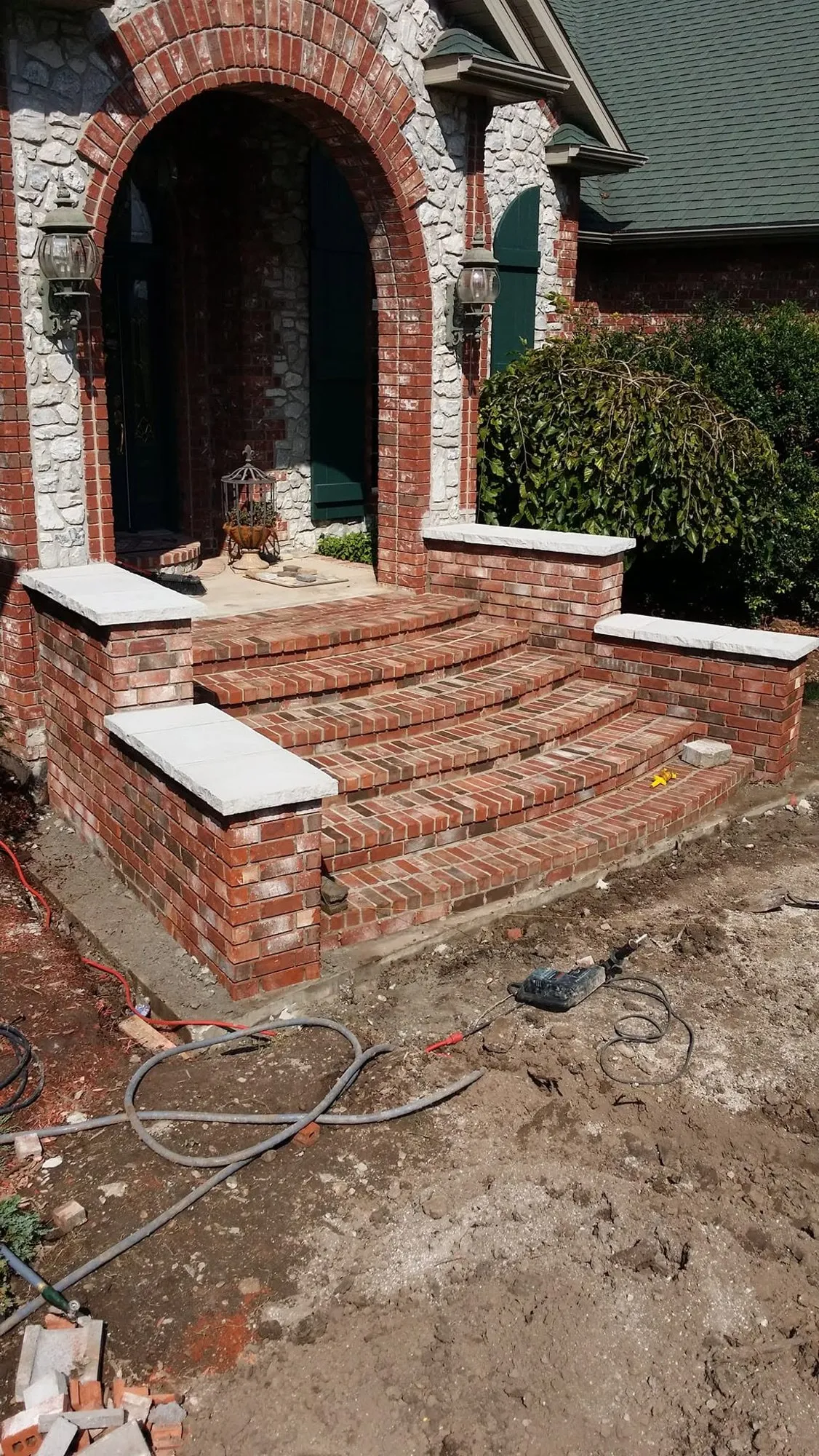 Curved red brick front steps with brick knee walls and chiseled stone caps leading to an arched brick and stone entry