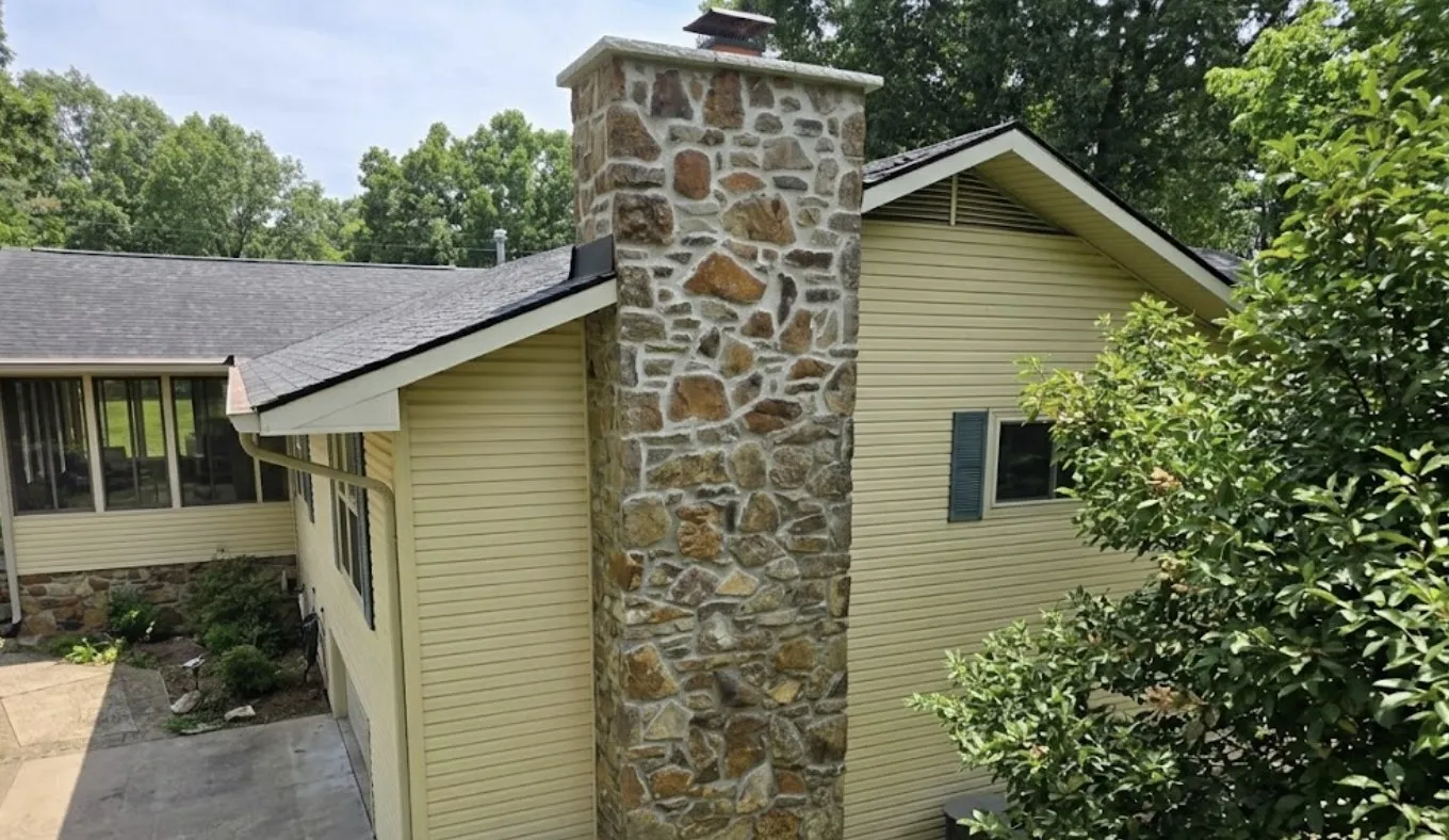 Rebuilt natural fieldstone chimney with a new cap rising beside yellow vinyl siding