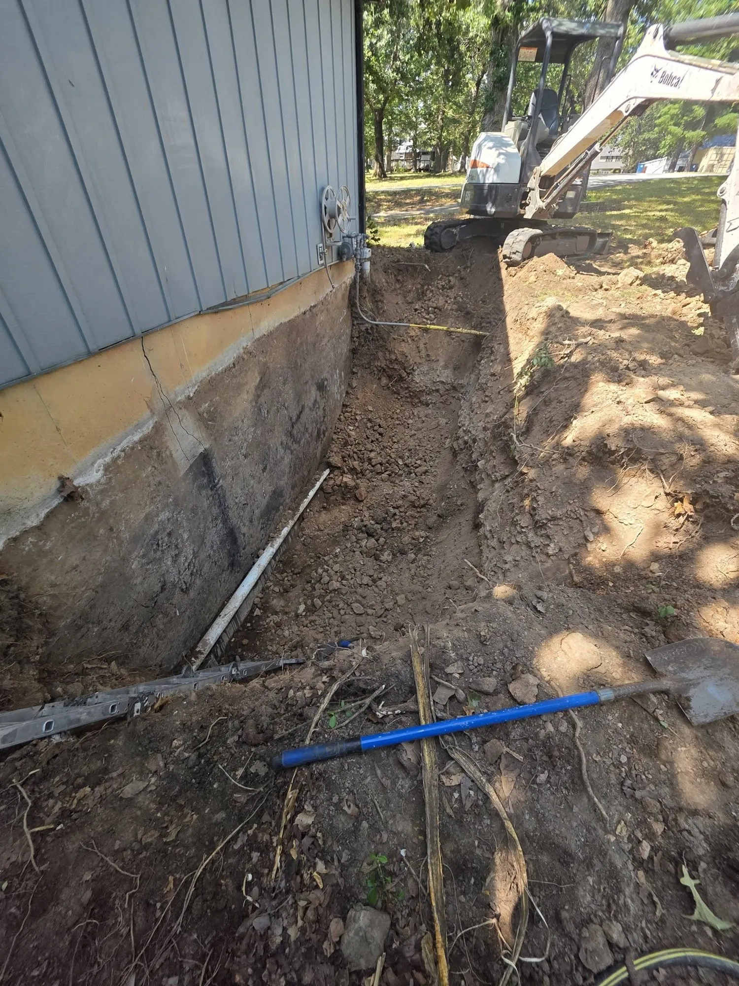 Long trench along a foundation wall with perforated drain pipe and a mini excavator