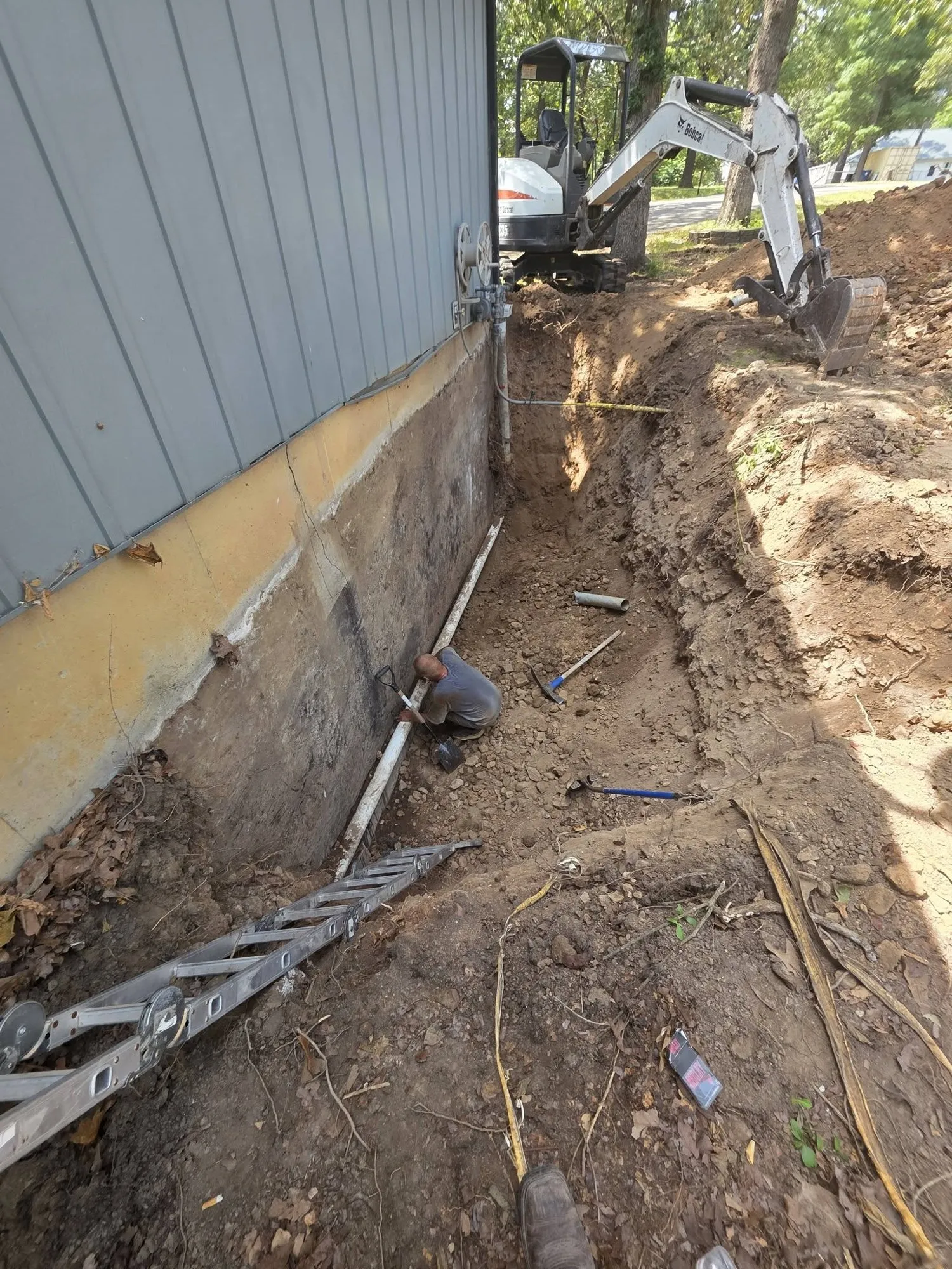 Excavated foundation wall with a visible crack and new drain pipe as a crew works in the trench