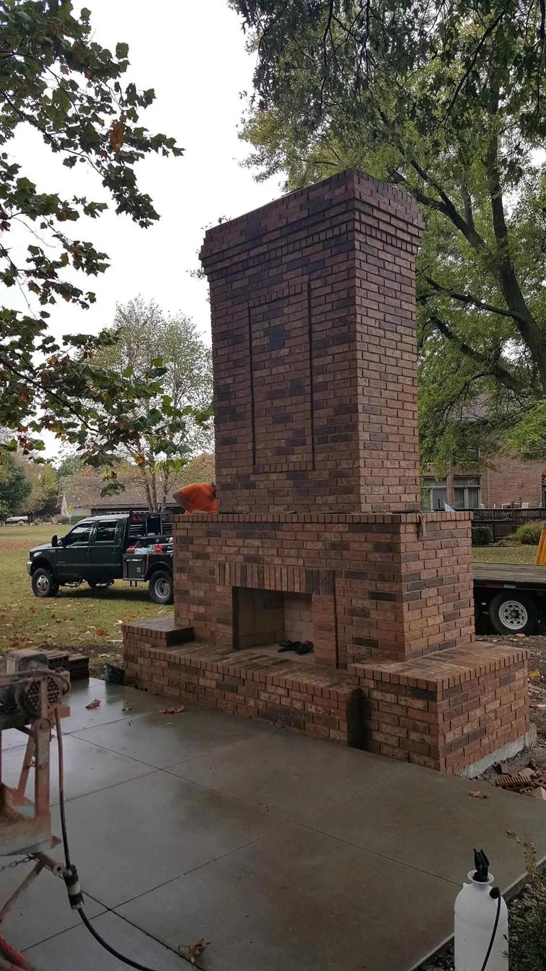 Tall freestanding brick outdoor fireplace and chimney with corbelled top and brick hearth wings on a new patio