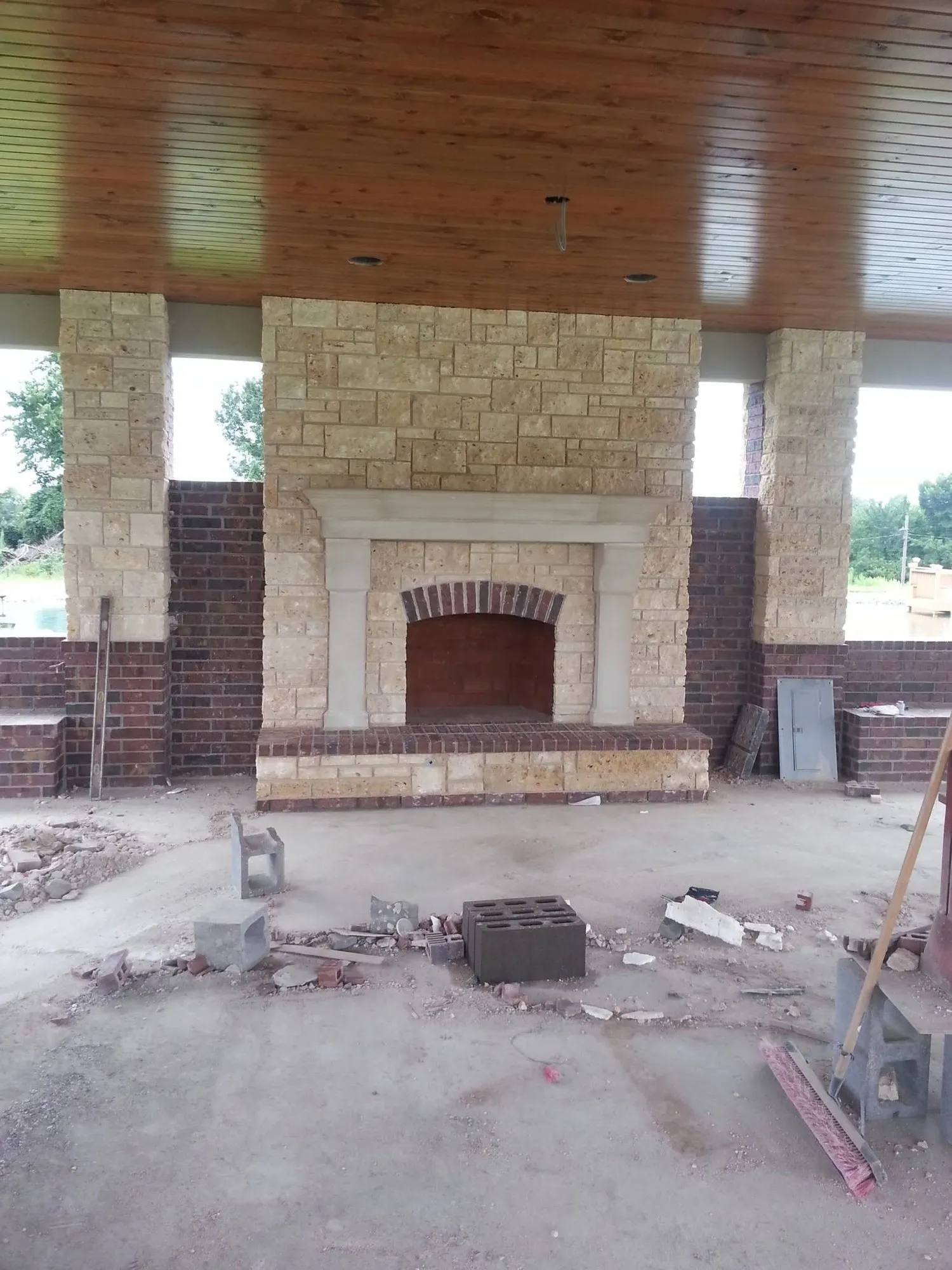 Outdoor limestone fireplace with cast stone mantel, brick arch and brick knee walls under a covered pavilion