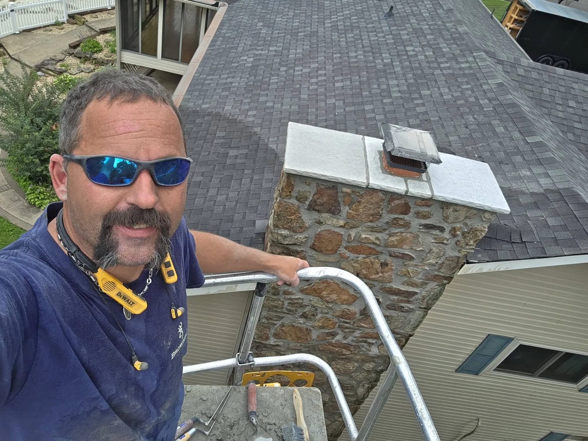 Chris, owner of CM Home Remedies, on a lift beside a repointed stone chimney with a new cap