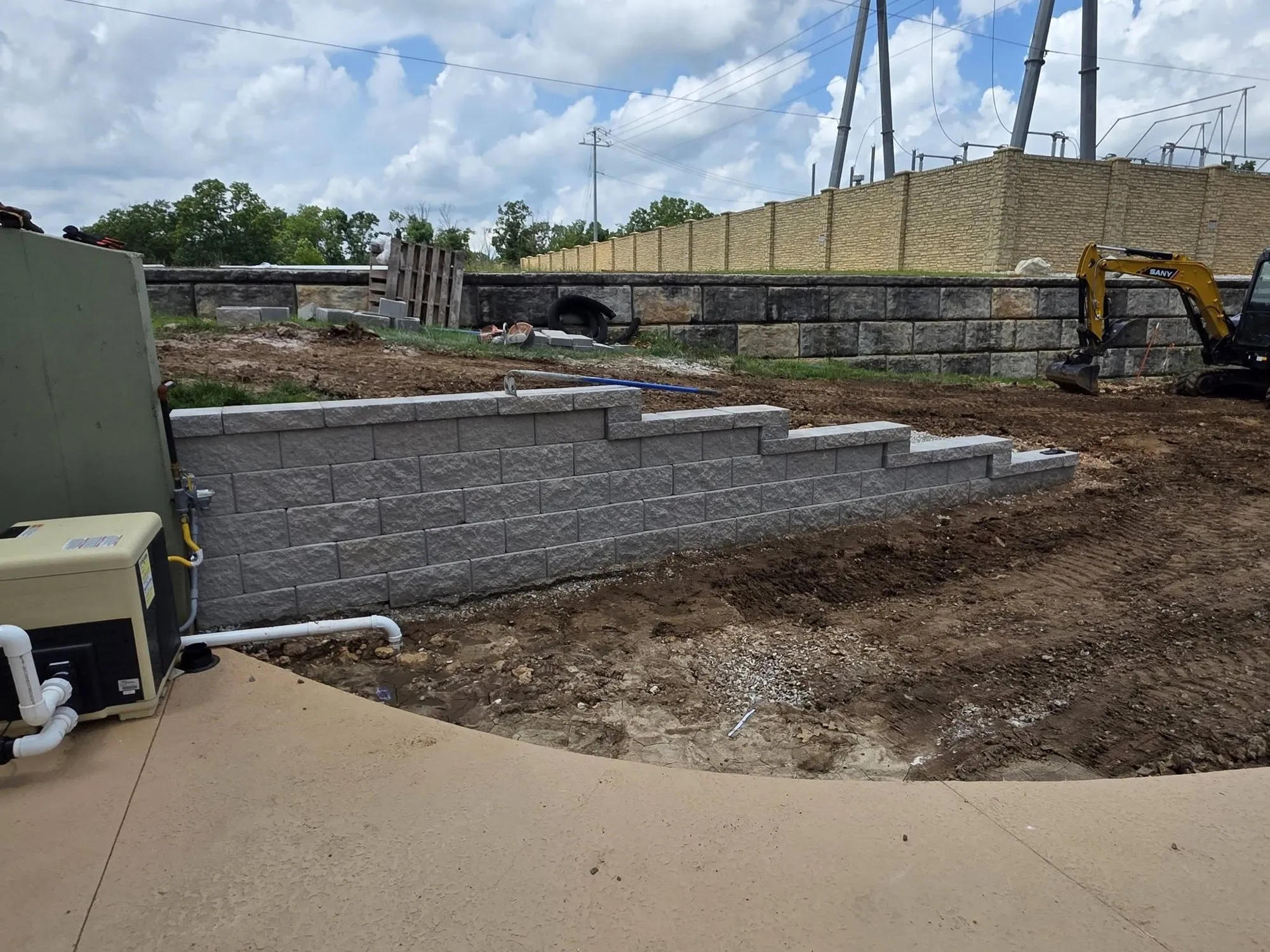 Gray segmental block retaining wall stepping down with the grade during construction beside a pool deck