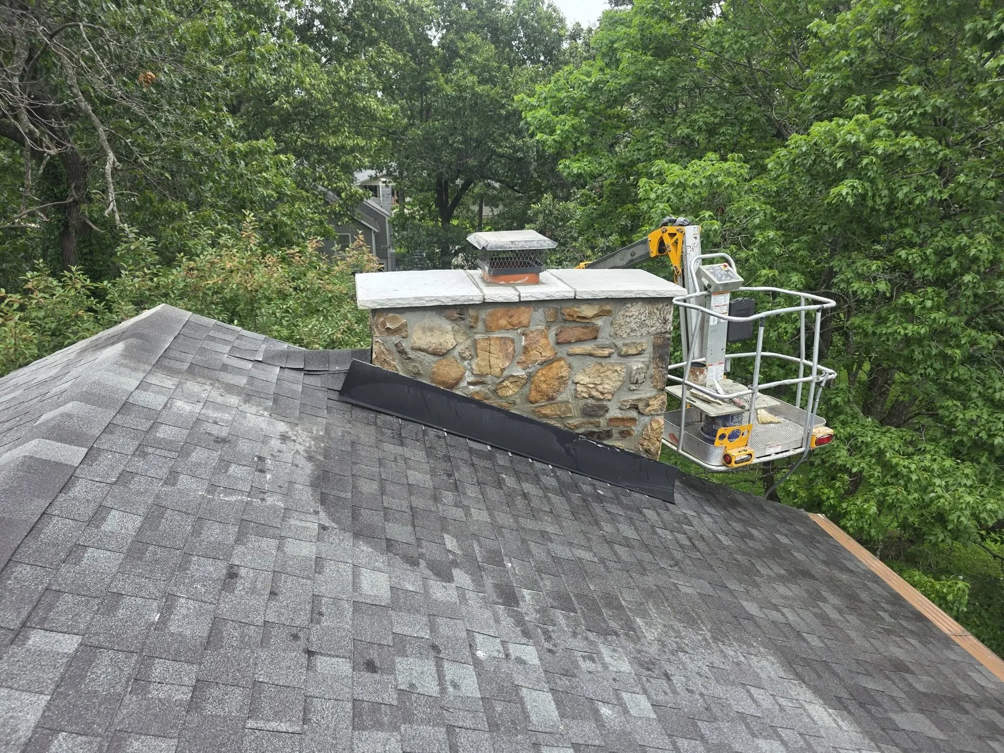Stone chimney on a shingled roof with new stone cap, chimney cover and step flashing