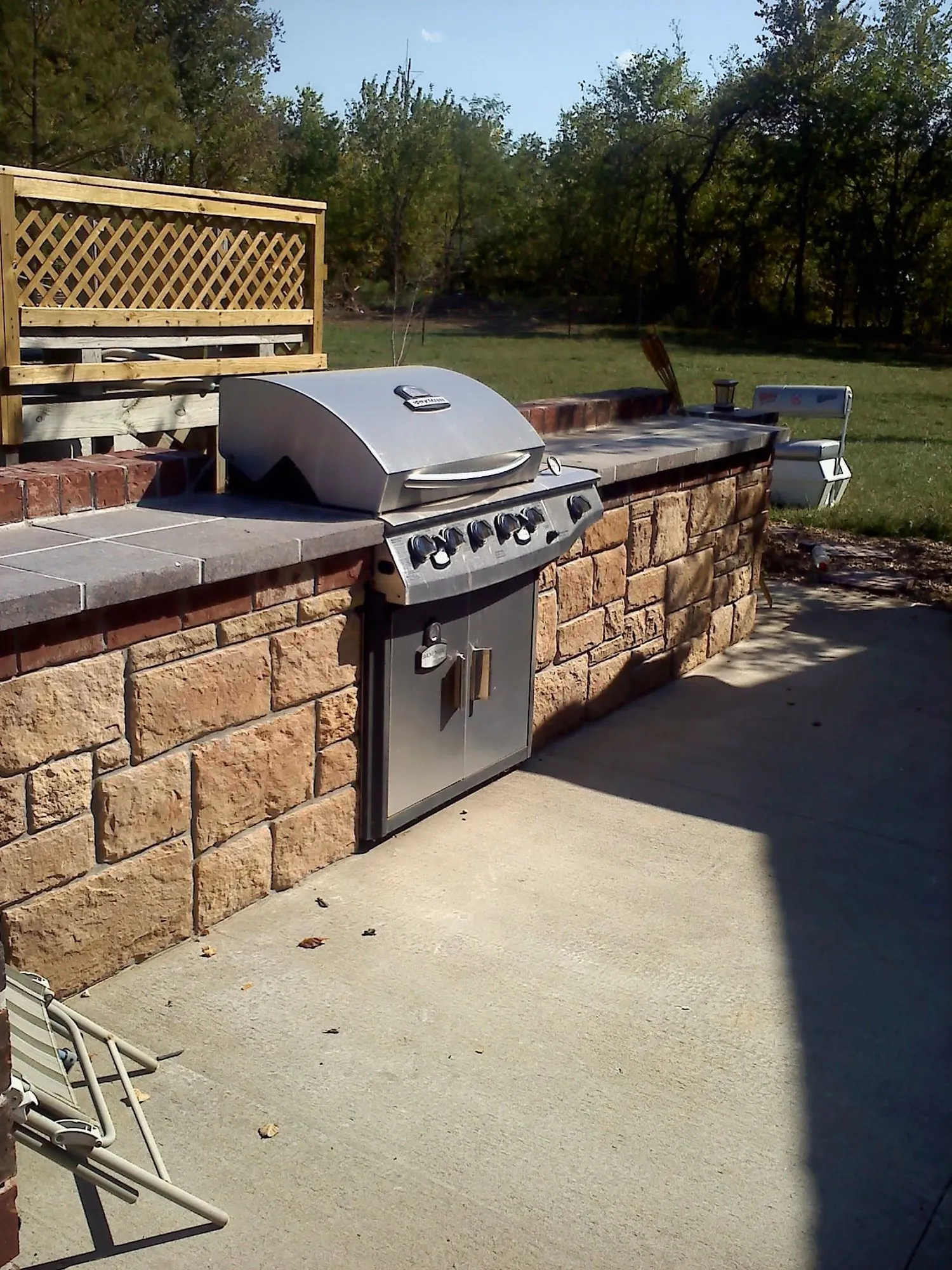 Outdoor grill island with tan stone veneer, brick accent course and tile countertop on a concrete patio