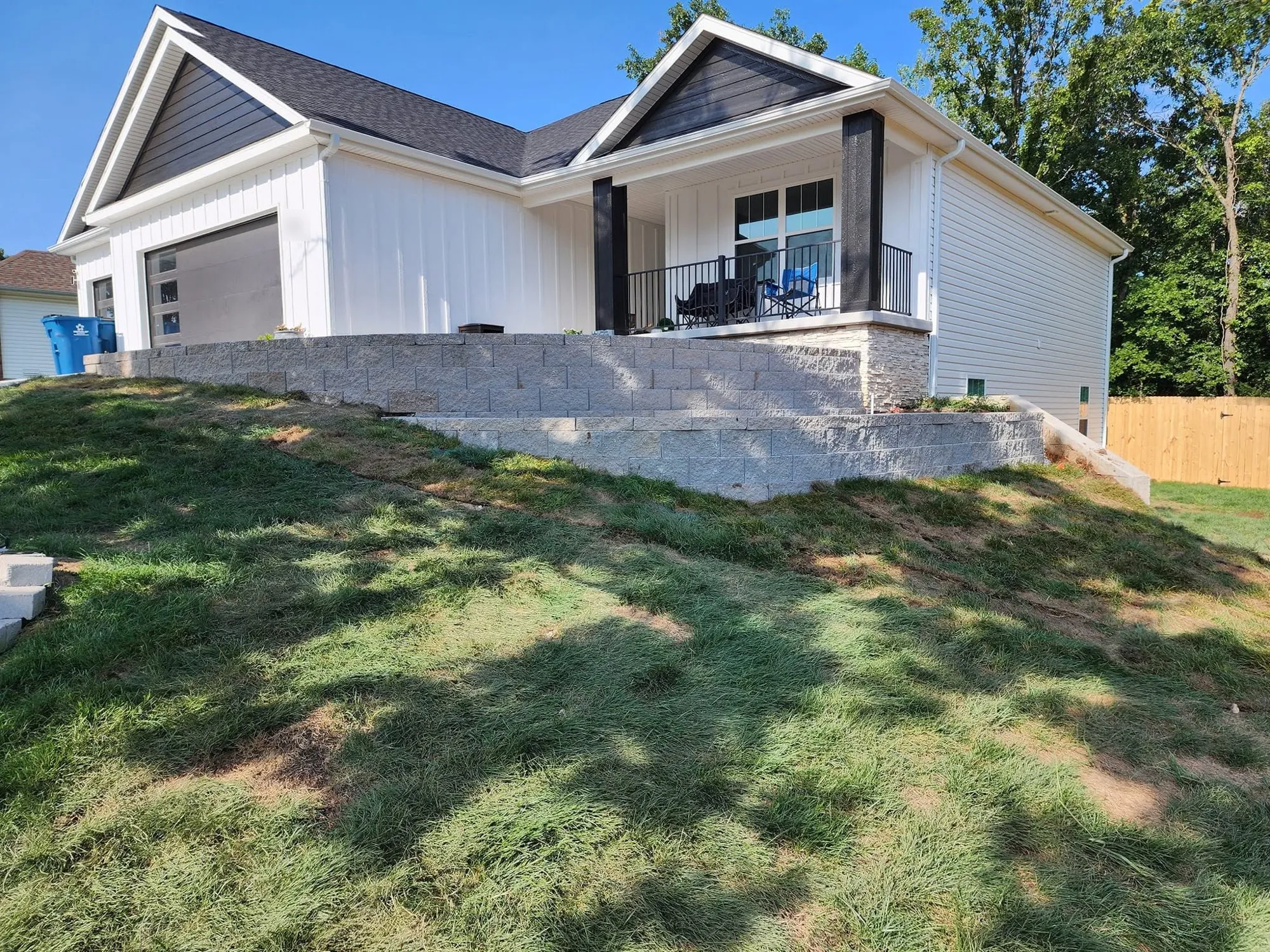 Two-tier segmental block retaining wall holding a sloped front yard below a new farmhouse-style home