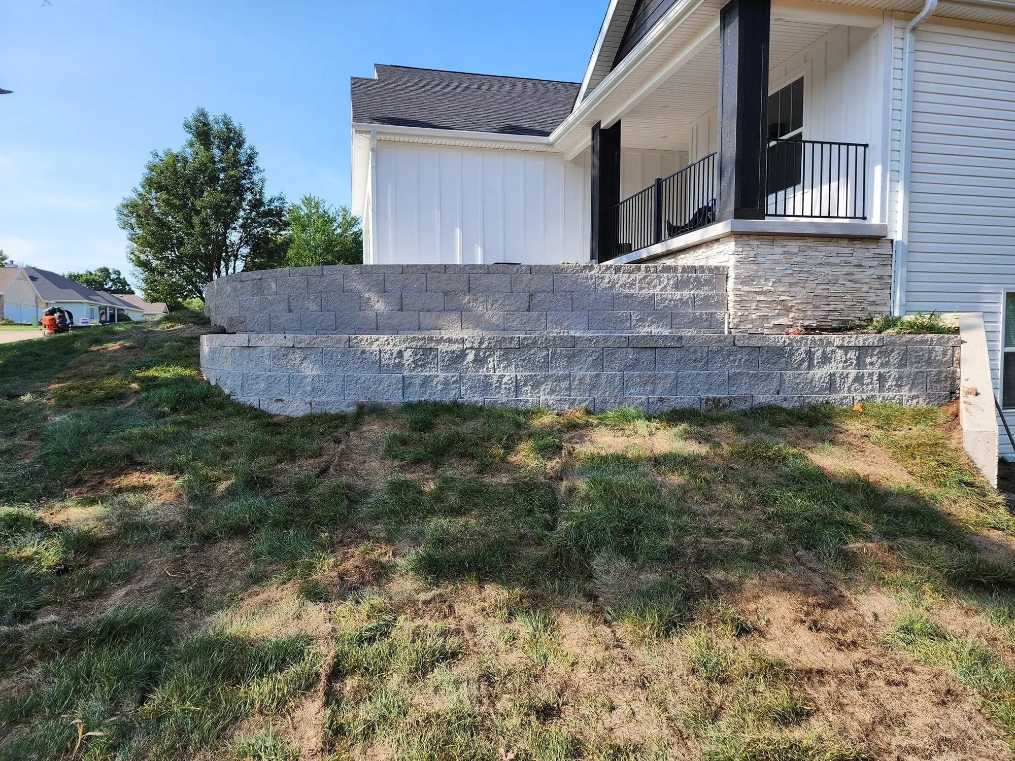 Curved two-level block retaining wall wrapping a front porch with stacked stone veneer
