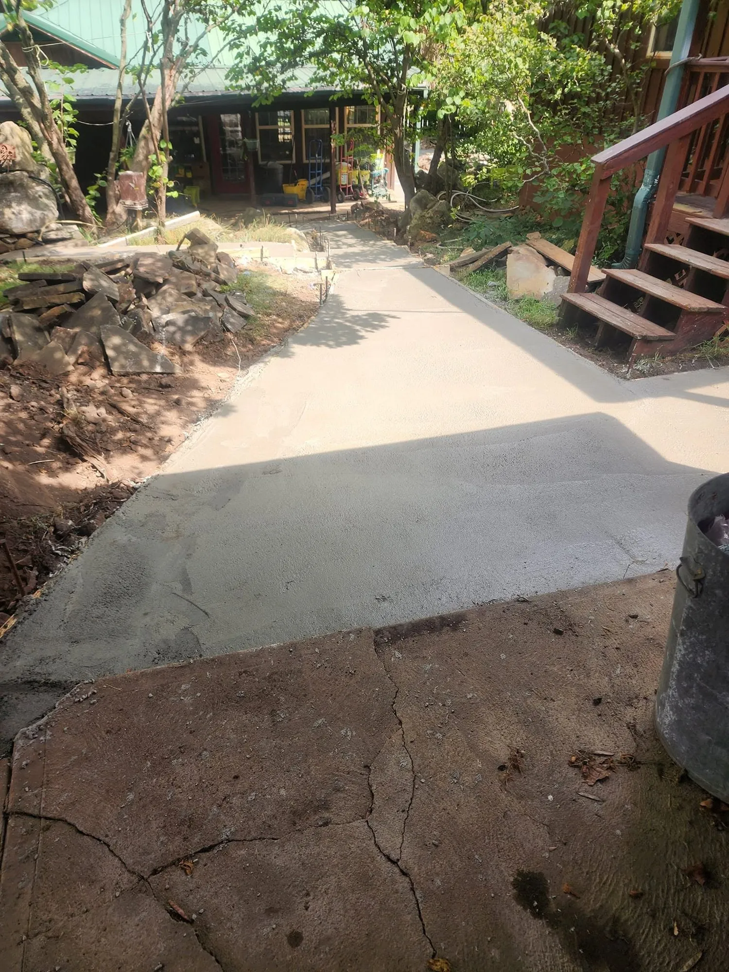 Freshly finished concrete walkway replacing an old flagstone path through a shaded backyard